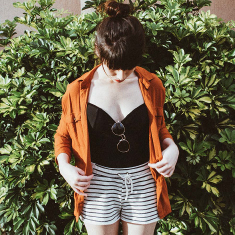 A woman in front of a bush wearing an orange jacket